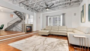 Un salón amplio con chimenea, un sofá modular, una escalera y un ventilador de techo.