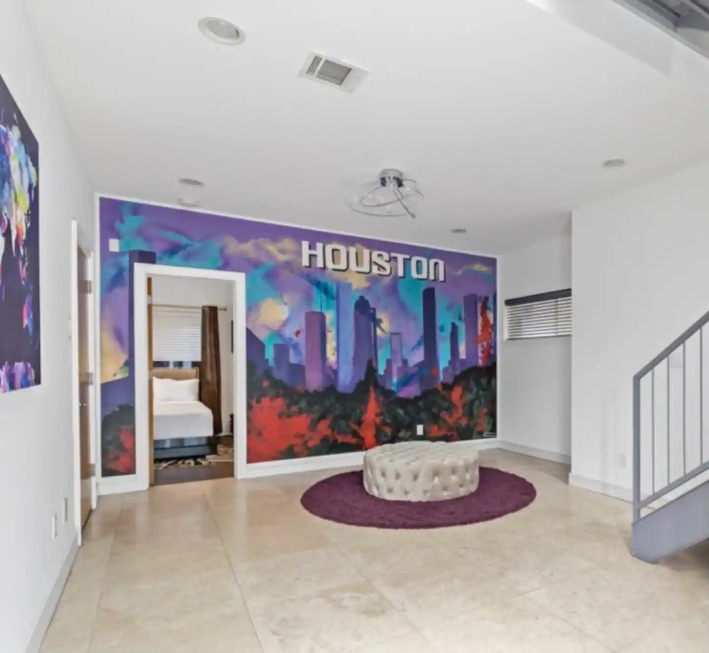 A modern hotel lobby with a cityscape mural, a round seating area, and a staircase.