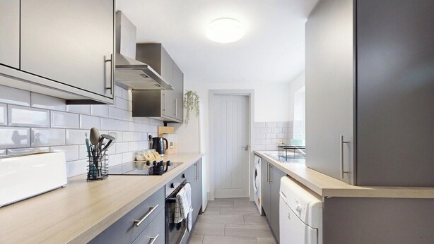 Une cuisine moderne avec des meubles gris, un plan de travail en bois, un four encastré et un lave-vaisselle.