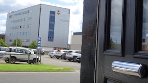 Ein Gebäude mit einer großen Schrifttafel, auf der "University of Sunderland" steht, und einem Parkplatz mit mehreren Autos.