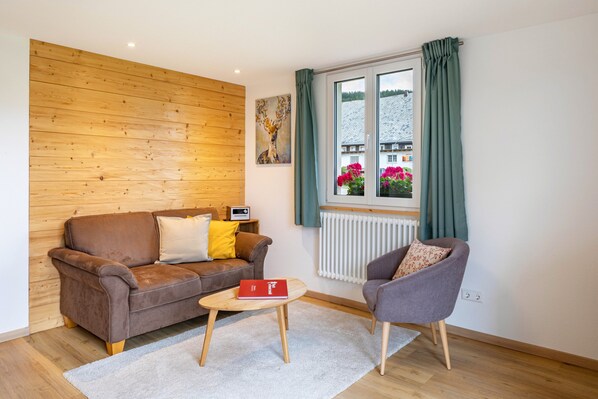 Une pièce chaleureuse avec un canapé en cuir marron, un fauteuil gris, une petite table basse en bois et une fenêtre avec des rideaux.