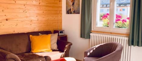A living room with a brown sofa, a grey armchair, a small wooden coffee table, and a painting on the wall.