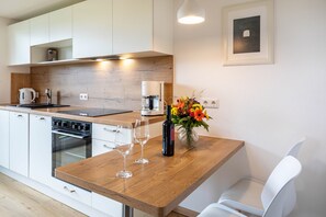 Une cuisine moderne avec des meubles blancs, un plan de travail en bois, une machine à café, deux verres à vin et un vase avec des fleurs.