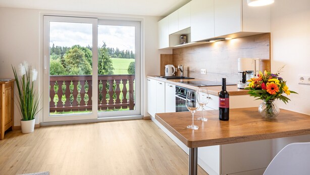 A modern kitchen with a wooden countertop, a dining area with a table, and a view of a balcony with a wooden railing. - Apartment 'Gästehaus Steiert Fewo Kuhbergblick' with Mountain View, Shared Garden and Wi-Fi (Lenzkirch)