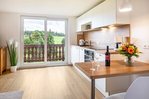 A modern kitchen with a wooden countertop, a dining area with a table, and a view of a balcony with a wooden railing.