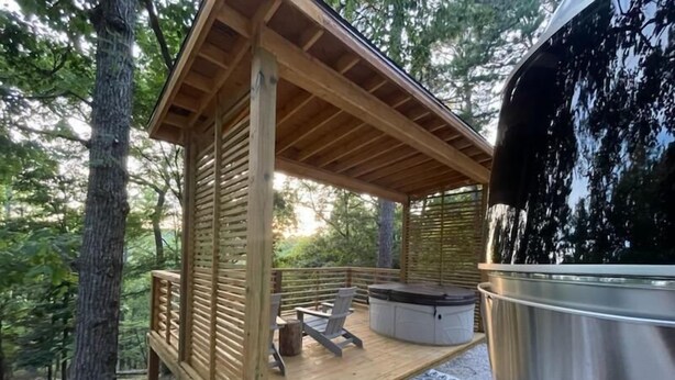 Une terrasse en bois avec un jacuzzi, un barbecue et un tapis à motifs.