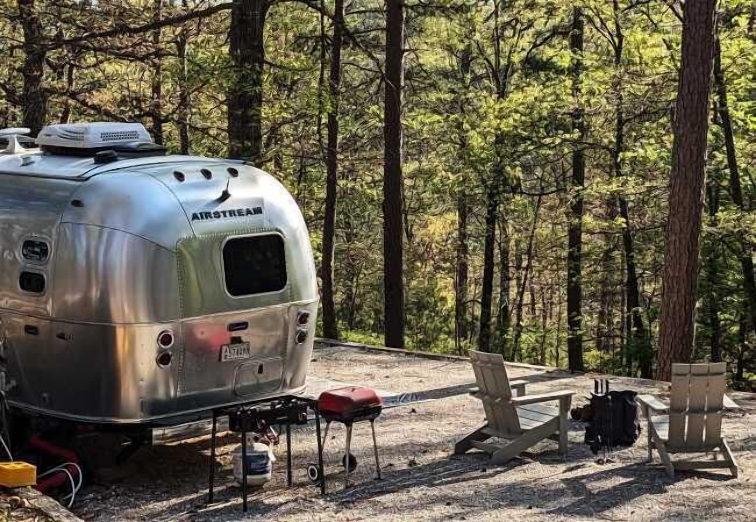 A silver trailer with "AIRSTREAM" branding parked in a forest.