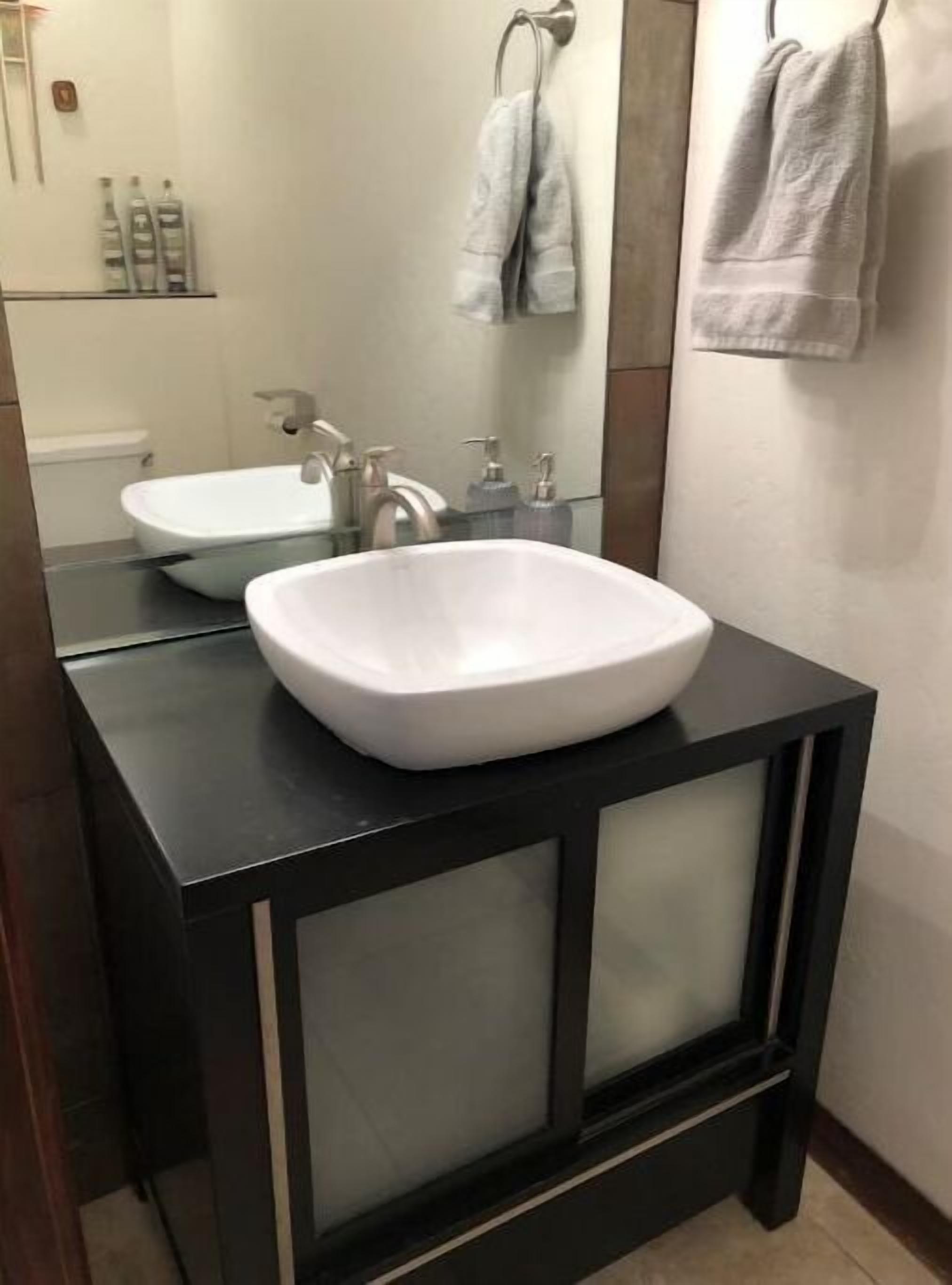 Une salle de bain moderne avec un lavabo blanc, un meuble-lavabo noir et un miroir au-dessus du lavabo.