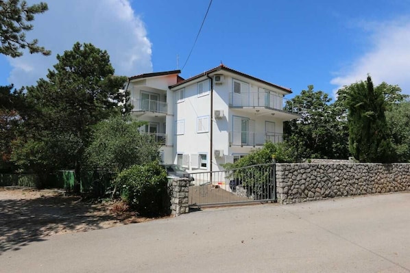 A multi-story building with balconies, a stone wall, and a paved driveway.