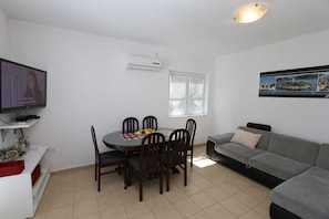 Una sala de estar con una mesa de comedor, sillas, un sofá, un televisor y una ventana con persianas.