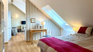 Una camera da letto con soffitto spiovente, una scrivania con sedia, un letto con coperta rossa e una TV sullo sfondo.