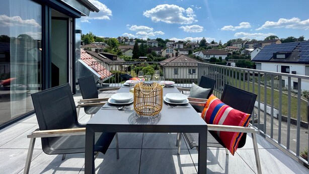 Un balcone con un tavolo apparecchiato per mangiare, sedie e vista sul quartiere.