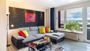 A modern living room with a sofa, a glass coffee table, a floor lamp, and a large window with a view. - Fewo Goldstadtblick – Spacious 125 m² Apartment with 2 Balconies & 3 Bedrooms for Groups & Families (Pforzheim)