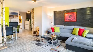 A modern living room with a grey sofa, a glass coffee table, and a dining area with a table and chairs. - Fewo Goldstadtblick – Spacious 125 m² Apartment with 2 Balconies & 3 Bedrooms for Groups & Families (Pforzheim)