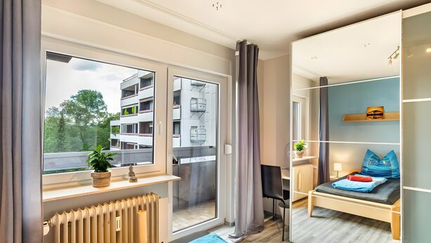A modern hotel room with a large window, a radiator, a bed, a desk, and a chair. - Fewo Goldstadtblick – Spacious 125 m² Apartment with 2 Balconies & 3 Bedrooms for Groups & Families (Pforzheim)