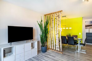 En moderne stue med et fladskærms-tv, en stueplante, et spiseområde med gul væg og en trævæg.