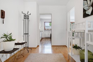A hallway with a coat rack, potted plants, a white shelf, and a view into a kitchen. - 2-room apartment 'Lieblingsnest' with great terrace, 3 km from Lake Constance, Wi-Fi (Lindau (Bodensee))