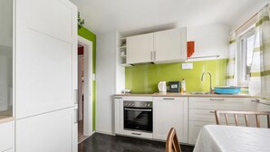 Une cuisine compacte avec des meubles blancs, une cuisinière, un évier et un coin repas comprenant une table et des chaises.