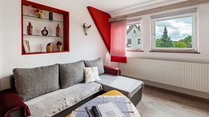 Un salon comprenant un canapé, une table basse, un mur d’accent rouge, une étagère en verre ornée d’objets décoratifs et une fenêtre offrant une vue agréable.