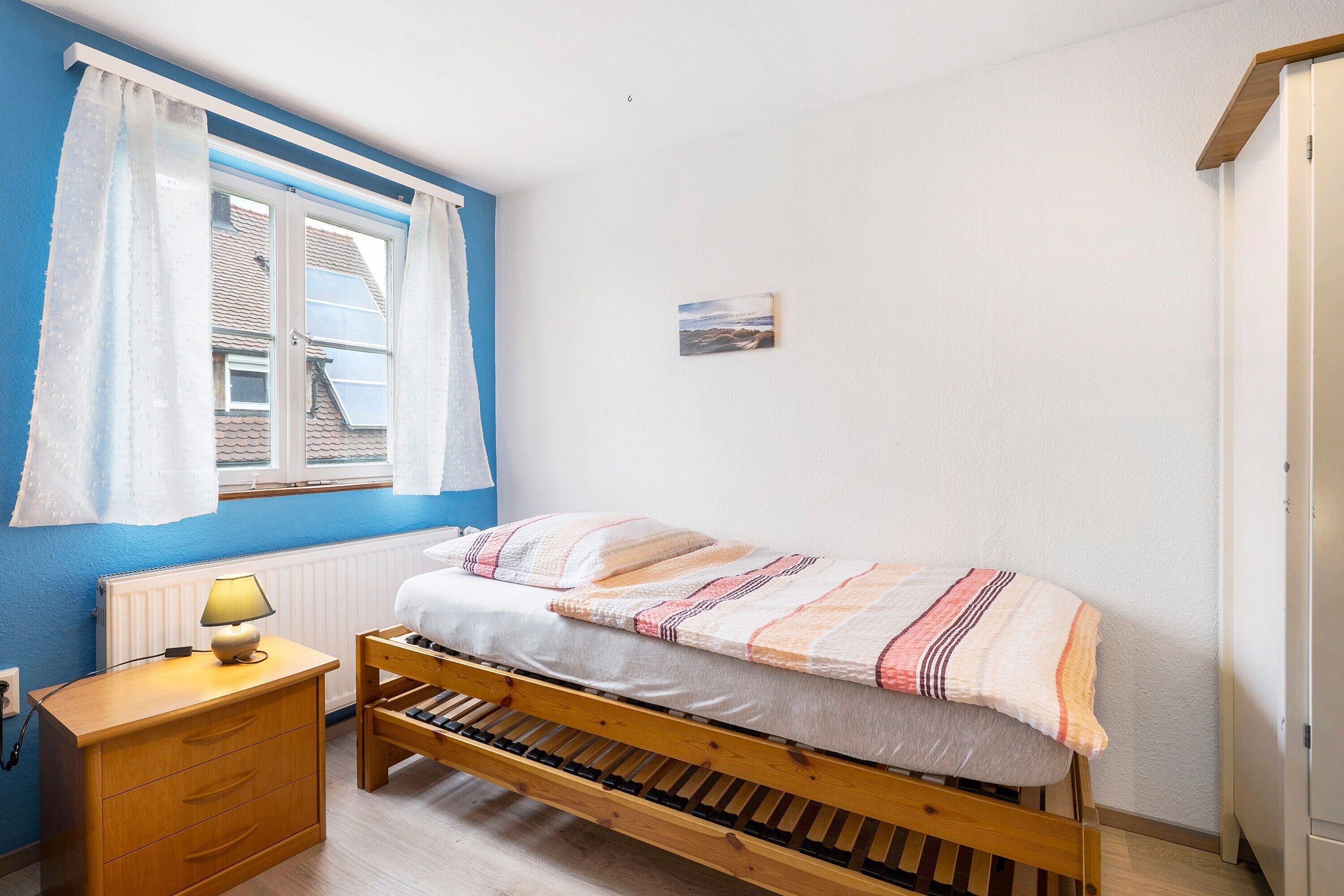 Quarto com cama de madeira, mesa de cabeceira com abajur, janela com cortinas e quadro pendurado na parede.