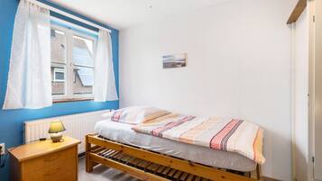 Quarto com cama de madeira, mesa de cabeceira com abajur, janela com cortinas e quadro pendurado na parede.
