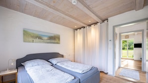 A bedroom with a bed, a nightstand, a painting, and a view of the outdoors.