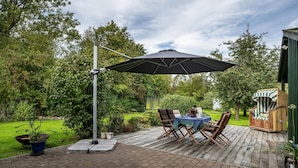 An outdoor patio with a table and chairs, a large umbrella, and a wooden deck.