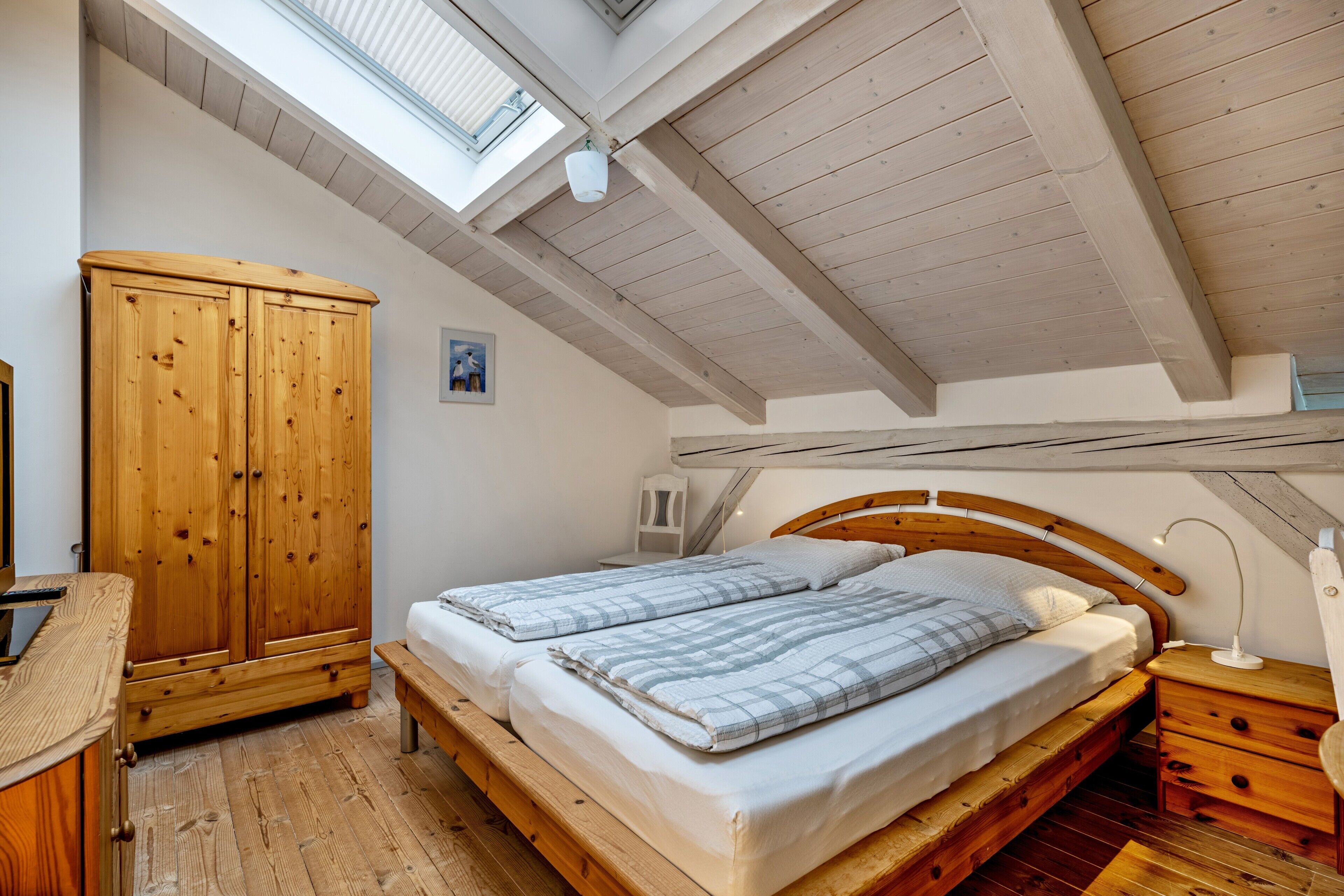 A bedroom with a wooden bed, a wooden wardrobe, a skylight, and a wooden ceiling.