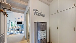Un pasillo con un armario, un cartel que dice 'Relax', un comedor con sillas y una mesa, y un televisor.