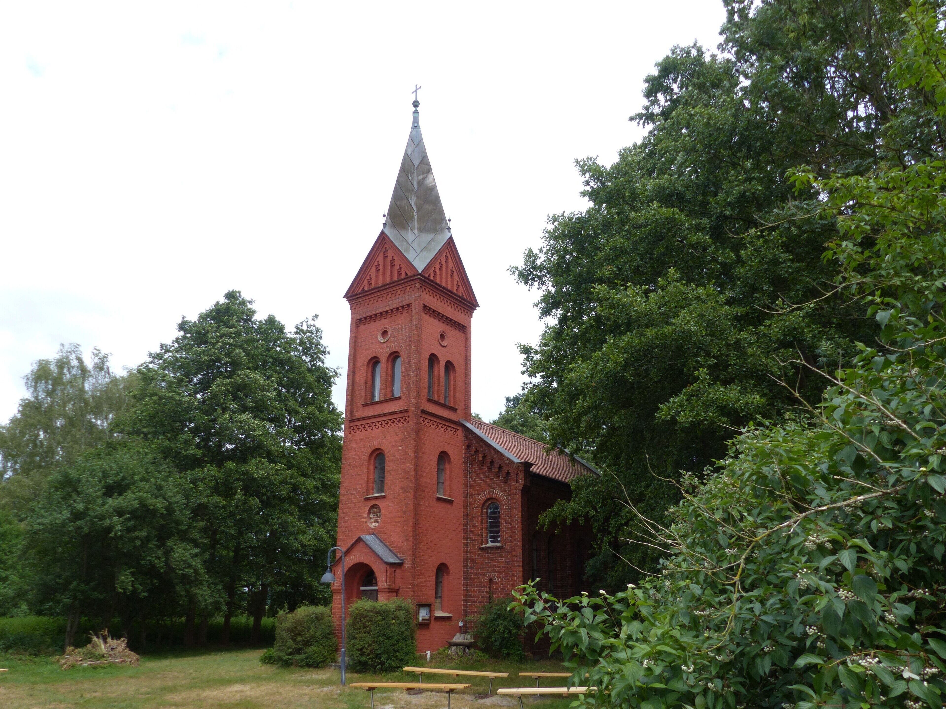Una chiesa in mattoni rossi con un campanile alto e una croce in cima, circondata dal verde.