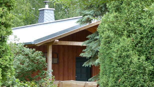A rustic cabin with a wooden exterior, a chimney, and a porch with a bench. - Holiday Home 'Jagdhaus Franz' with Terrace (Kloster Lehnin)