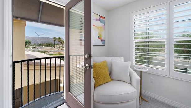 Une chambre moderne dotée d’une porte-fenêtre coulissante donnant sur un balcon, d’un canapé blanc agrémenté d’un coussin jaune et d’une petite table sur laquelle repose un livre.