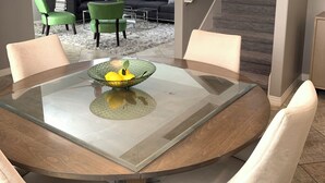 Un coin repas avec une table à plateau en verre, un saladier rempli de fruits et un ventilateur de plafond.