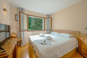 Un dormitorio con cama, un escritorio de madera, un televisor y una ventana con cortinas.