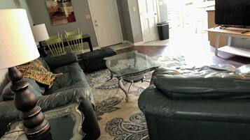 Un salon avec un canapé, une table basse en verre, un tapis à motifs et un téléviseur.