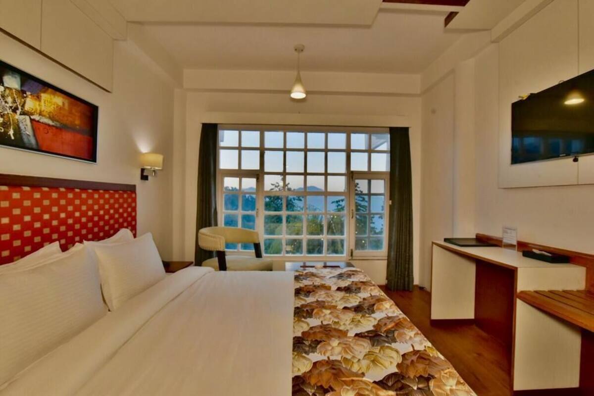 A hotel room with a large bed, a desk, a chair, a TV, and a window with a view.