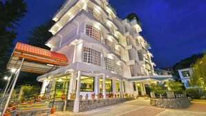 A multi-story hotel with a white facade, multiple balconies, and a well-lit entrance. - Hillcrest Resort by DLS Hotels (Shimla)