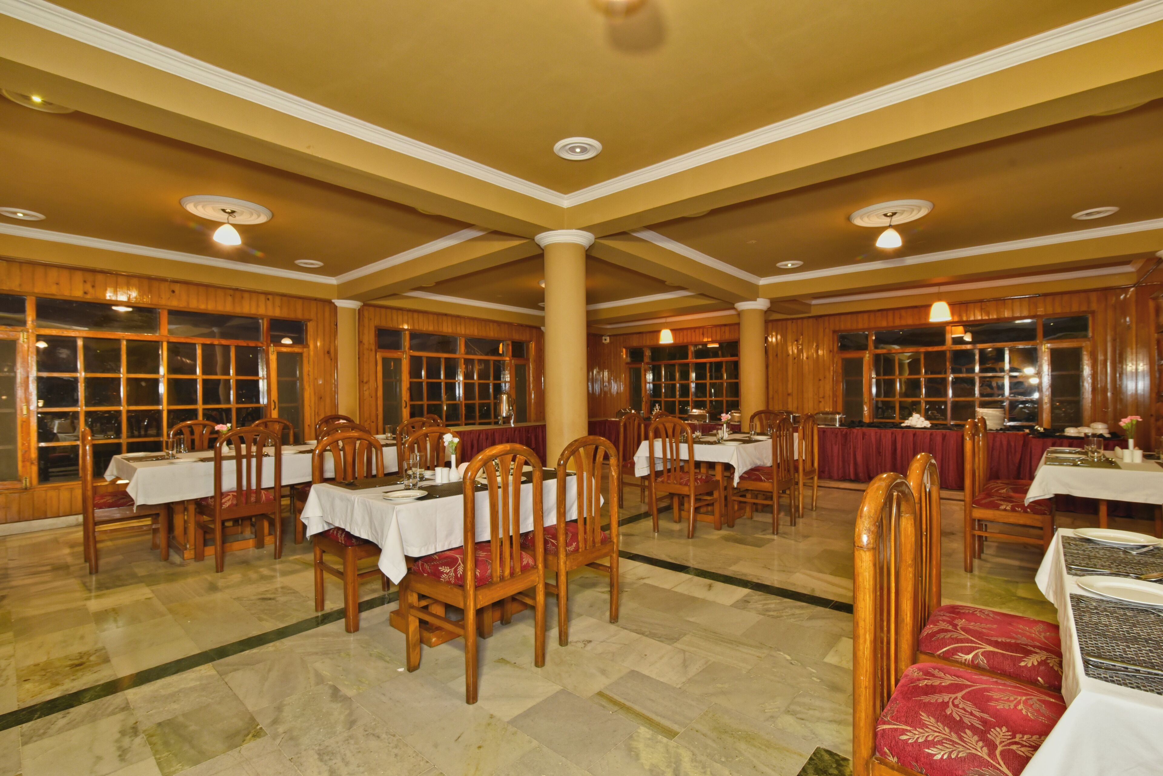 Un comedor con varias mesas y sillas, paneles de madera en las paredes y ventanas amplias.