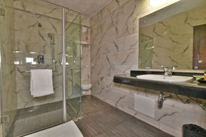 A modern bathroom with a glass-enclosed shower, a marble-tiled wall, a sink with a black countertop, and a mirror above the sink. - Hillcrest Resort by DLS Hotels (Shimla)