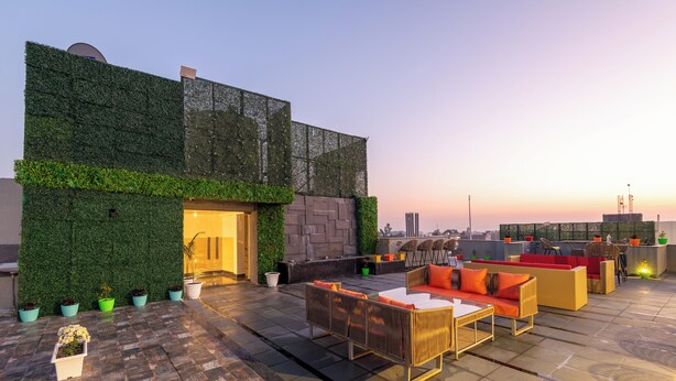 A rooftop patio with outdoor seating, a green wall, and a view of the city skyline at dusk. - Hillcrest Resort by DLS Hotels (Shimla)