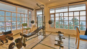 A gym with large windows, weightlifting equipment, and a bench. - Hillcrest Resort by DLS Hotels (Shimla)