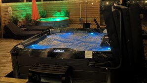 Un bain à remous doté d’une terrasse en bois, entouré de chaises longues et d’une clôture en bois.