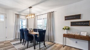 Un espace repas comprenant une table en bois, des chaises à revêtement sombre, un tapis à motifs et un luminaire suspendu moderne.