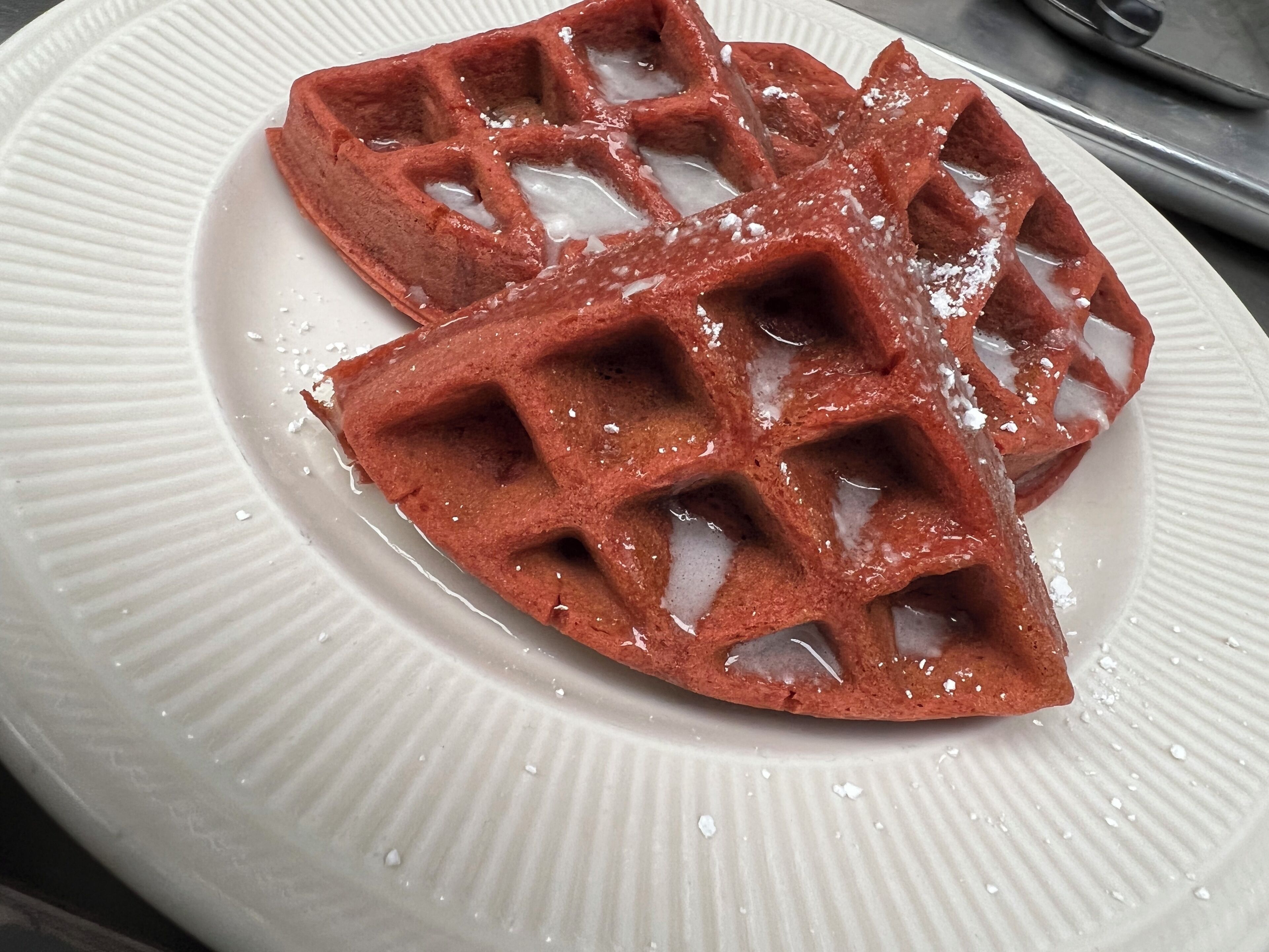 A waffle with syrup and powdered sugar on a white plate.