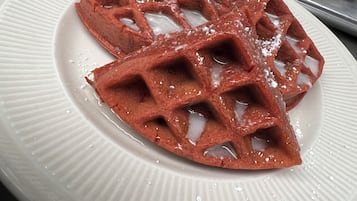 A waffle with syrup and powdered sugar on a white plate.