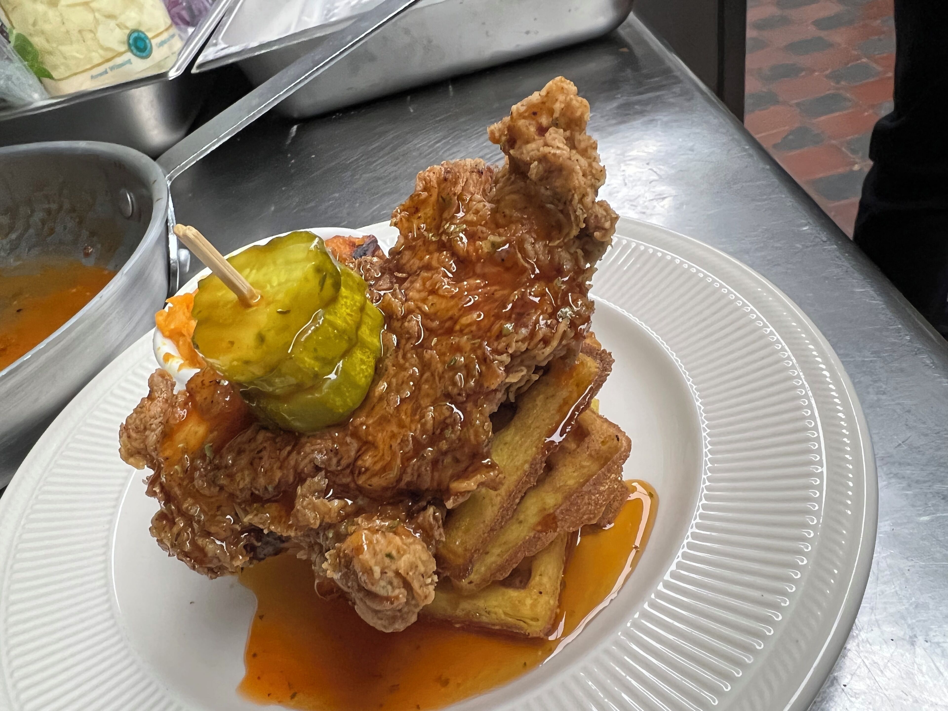 A plate with fried chicken, fries, and a pickle on a white paper plate.