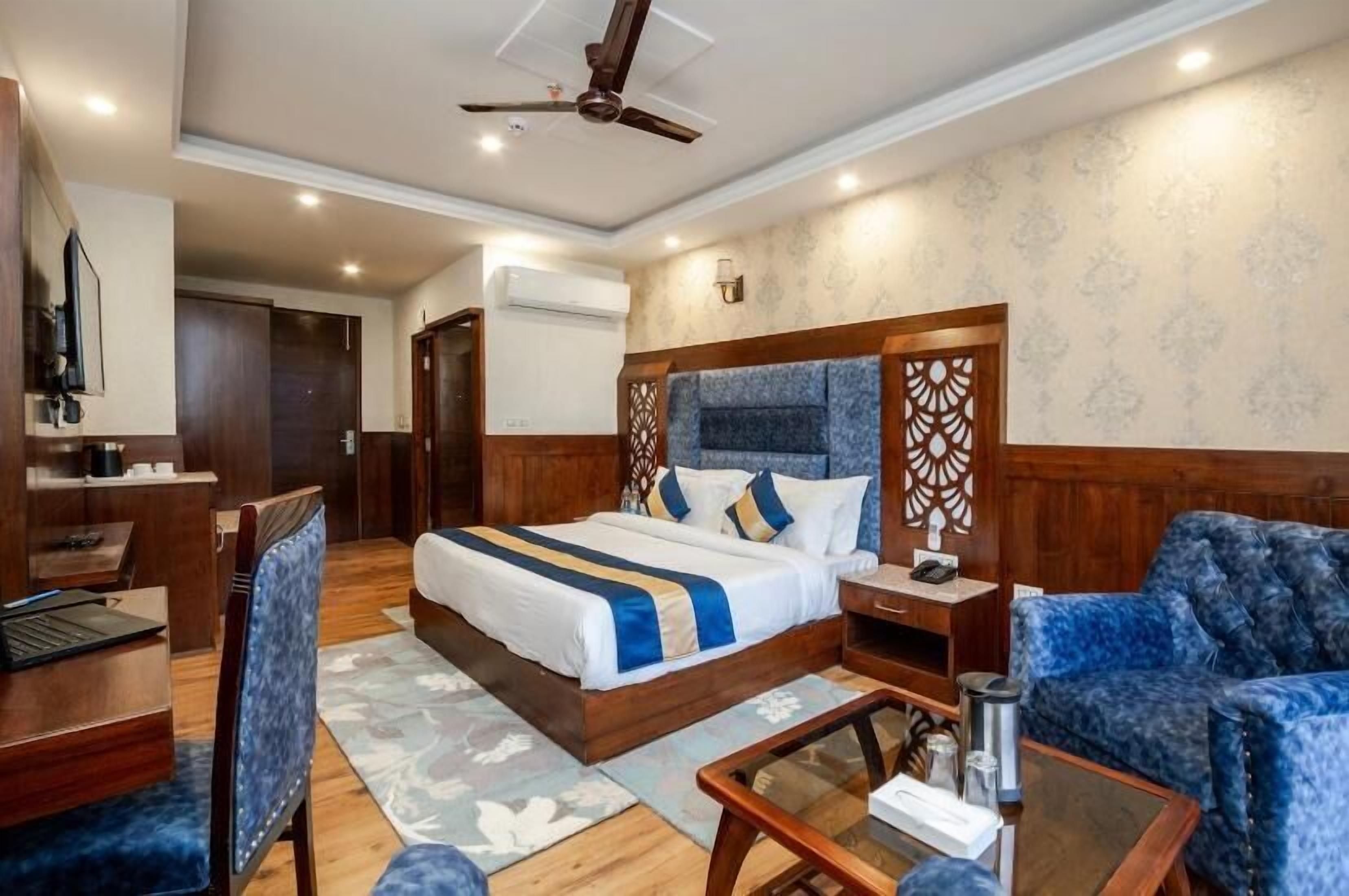 A hotel room with a large bed, a desk, a chair, a sofa, a coffee table, and a ceiling fan.