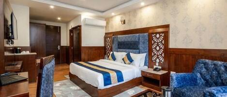 A hotel room with a large bed, a desk, a chair, a sofa, a coffee table, and a ceiling fan.