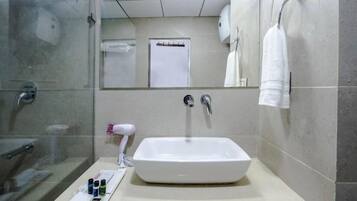 A bathroom with a large white sink, a glass shower enclosure, and a mirror with a towel rack.