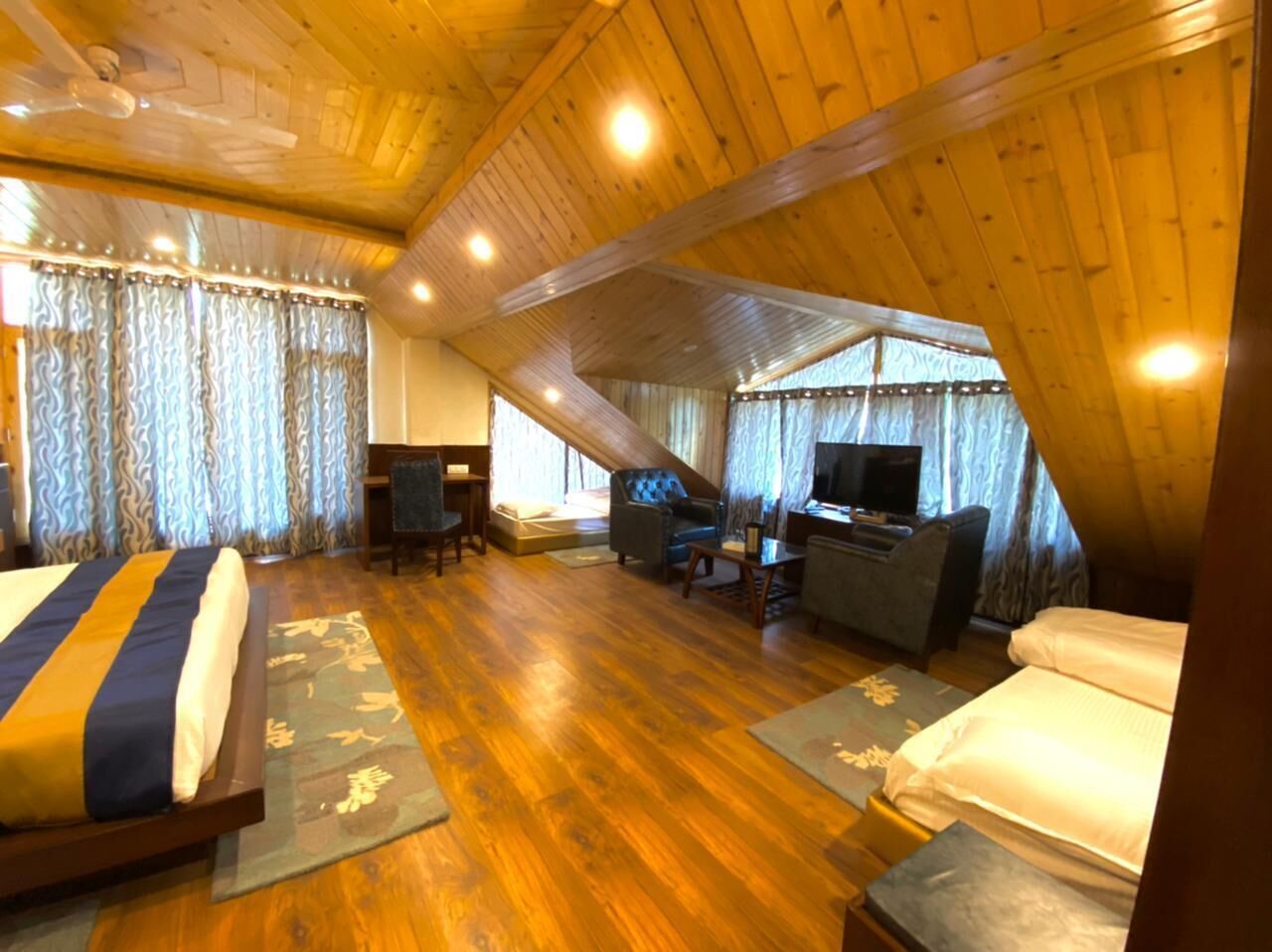 A cozy attic bedroom with a wooden ceiling, a bed, a desk with a TV, and a chair.